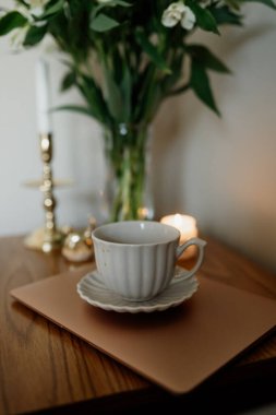 Bir buket çiçek, bir fincan çay ya da masada süt ve şekerli kahve. Ev konforu ve minimalizm gibi hissettiriyor. Estetik. Sonbahar estetiği. Altın bir şamdanda mum.