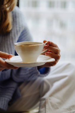 Kız elinde bir fincan kahve ya da sütlü çay ve rahat bir rahatlama atmosferi tutuyor. Estetik