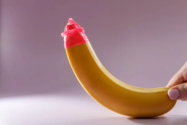 Condom on a banana on a colored background. Pink Condom. Safe sex concept