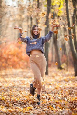 Sonbahar ormanına düşen yaprakları atan neşeli, genç bir kadın.