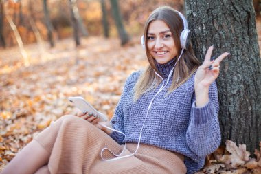 Güz ormanlarında müzik kulaklıklarıyla müzik dinleyen güzel bir kadın.
