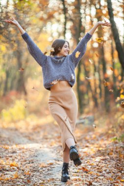 Sonbahar ormanına düşen yaprakları atan neşeli, genç bir kadın..