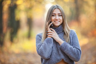 Sonbahar ormanında, sıcacık kazaklı tatlı bir kadın telefonda konuşuyor.