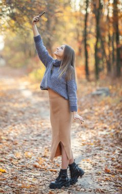 Sıcak süveter giyen hoş bir genç bayan sonbahar ormanında telefona cevap verir. Zayıf cep telefonu şebekesi