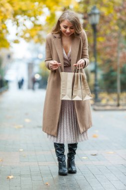Pardösülü mutlu kadın dışarıda alışveriş torbaları tutuyor, sonbahar alışverişi.