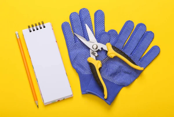 Garden pruner with work gloves and notebook on a yellow background. Flat lay. Top view
