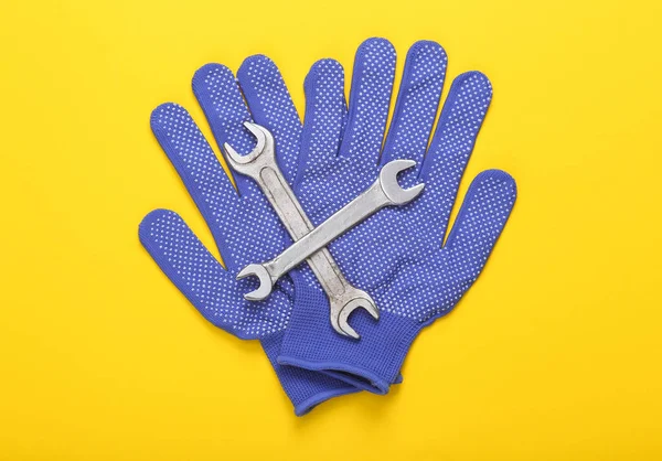 Job mechanic concept. Work gloves with wrenches on a yellow background