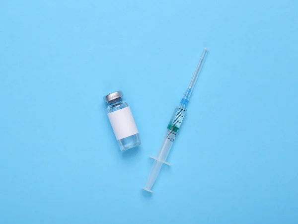 ブランドと青の背景に注射器のための空白のラベルを持つワクチンボトル — ストック写真