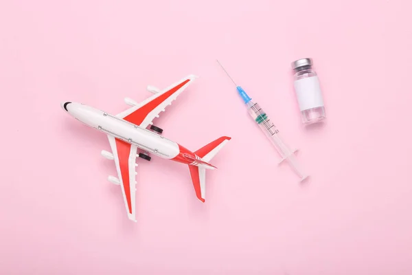 Vaccination, travel concept. Airplane with a bottle of vaccine and a syringe on pink background