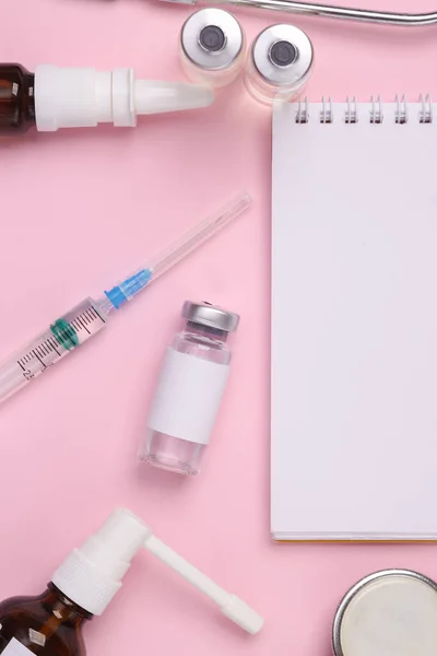 Flat lay composition of notebook with medicines on a pink background. Top view