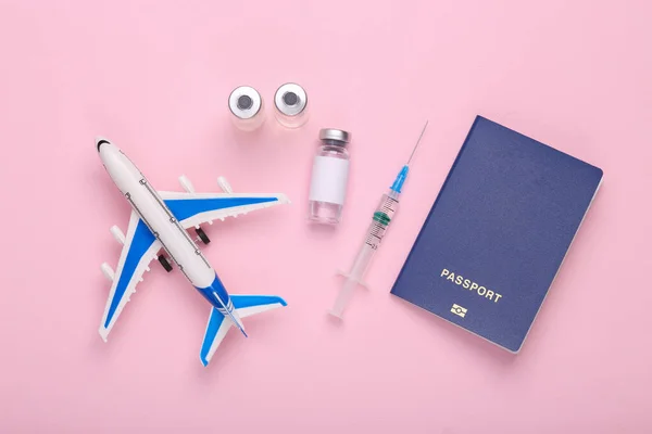 Vaccination, travel concept. Airplane with a bottle of vaccine and a syringe, passport on pink background