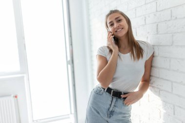 Parlak bir odada genç beyaz bir kadın telefonda konuşuyor.