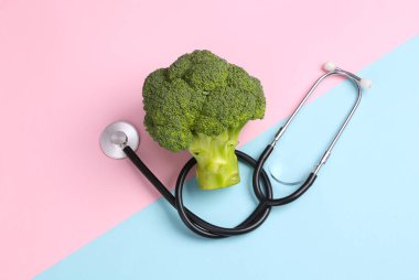 Sağlıklı gıda konsepti. Pembe mavi arka planda steteskoplu brokoli. Üst görünüm