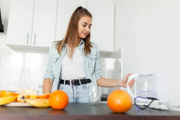 Young woman turns on the electric kettle in the kitchen