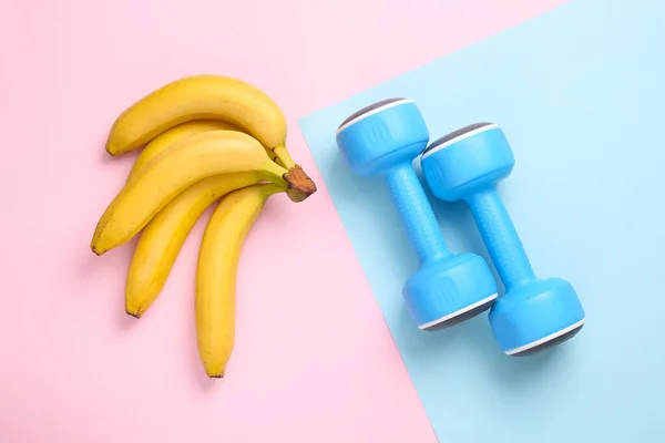 Fitness, healthy food concept. Dumbbells with bananas on a blue-pink pastel background. Top view