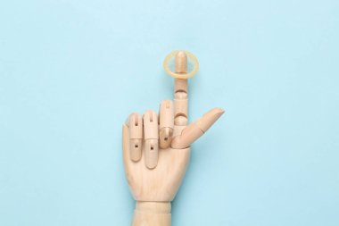 Ahşap bir elin parmağında kondom, mavi arka plan.