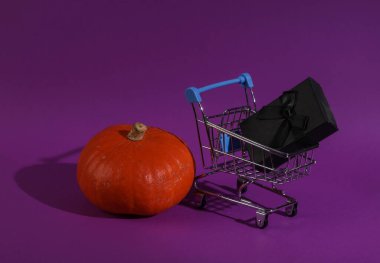 Mor arka planda hediye kutusu ve balkabağı olan alışveriş arabası. Cadılar Bayramı indirimi