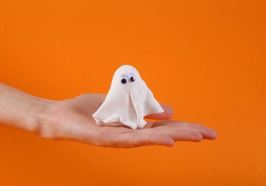 Avucunun içinde turuncu arka planda küçük bir plastik hayalet. Cadılar Bayramı konsepti