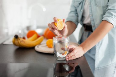 Kadın mutfakta bir bardak suya limon sıkıyor. Sağlıklı gıda konsepti. Vitaminler, antioksidanlar