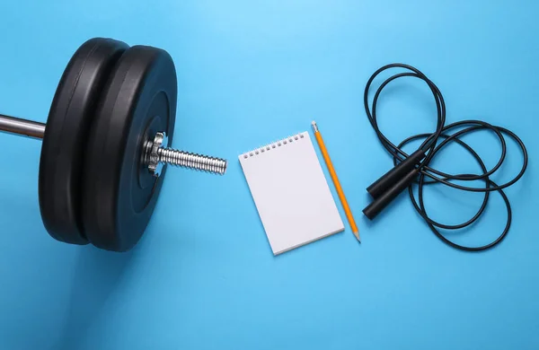 Drawing up a training program. Bodybuilding and fitness. Barbell with a notepad and a jump rope on a blue background. top view