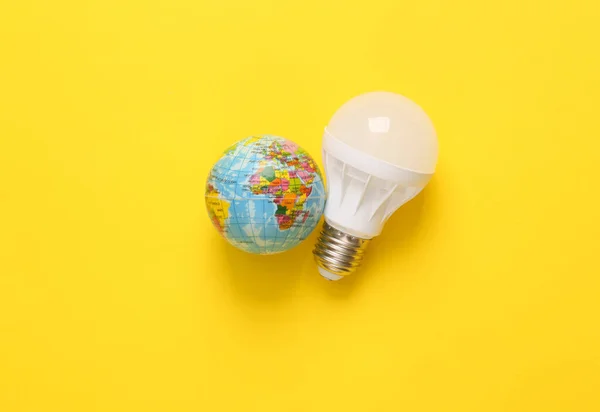 Led light bulb with a globe on a yellow background. Eco concept. Top view