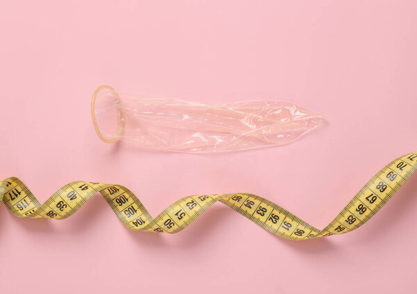 Used condom with measuring tape on pink background