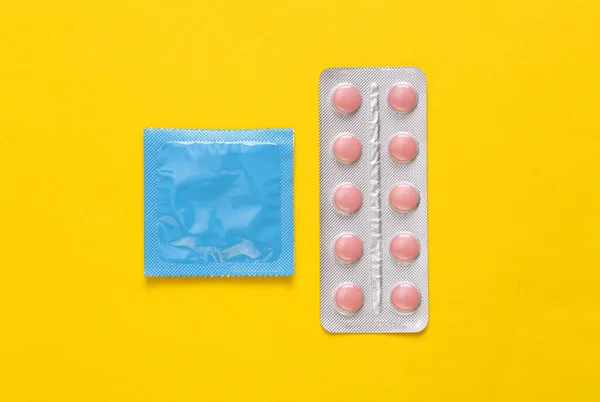 Condoms packaging and blister of contraceptive pills on yellow background