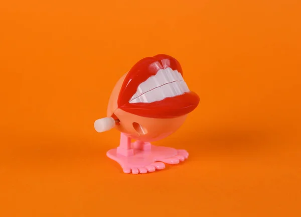 橙色背景下的玩具怪物唇之间的钟表 — 图库照片