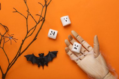 Cadılar Bayramı dekoru, yüzü olan şekerlemeler ve turuncu zemin üzerinde örümcek, yarasa, kukla eli olan kuru dallar. Düz yatıyordu.