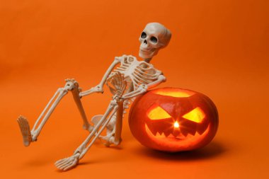 Cadılar Bayramı balkabağı kafalı balkabağı feneri yanan mumlar ve turuncu arka planda iskelet. Yaratıcı cadılar bayramı natürmortu