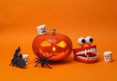 Cadılar Bayramı balkabağı kafalı balkabağı feneri yanan mumlar ve turuncu arka planda dekorasyon temalı. Yaratıcı cadılar bayramı natürmortu