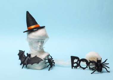 Mavi arka planda hala Cadılar Bayramı dekoru var. Cadı şapkası ve mavi arka planda Cadılar Bayramı dekoruyla sarılı antik bir heykel.