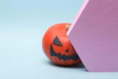 Korkunç Cadılar Bayramı balkabağı mavi arka planda geometrik şekillerin arkasına saklanır.