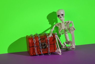 Korsan sandığı, yeşil-mor arka planda bir iskelet.