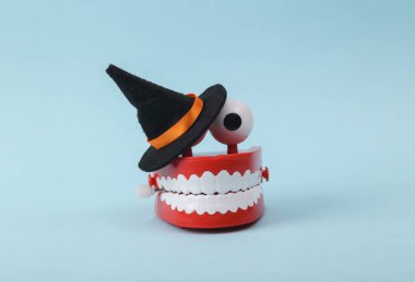 Funny toy clockwork jumping teeth with eyes and witch hat on blue background. Halloween still life