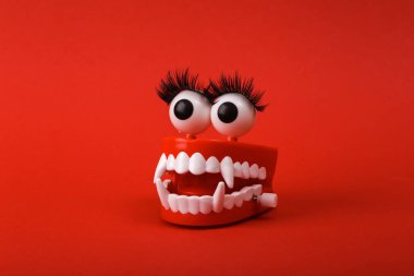 Funny toy clockwork jumping monster teeth with eyes and false eyelashes on red background. Beaty concept
