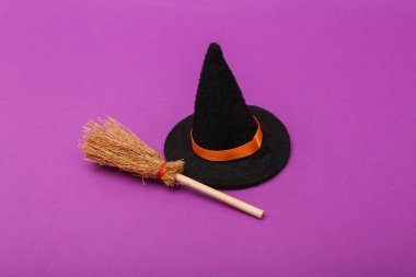 Halloween decor. Witch hat with broom on purple background
