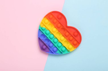Pop it sensory rainbow antistress heart shaped toy on pink blue background