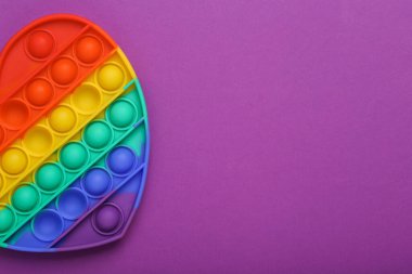 Pop it sensory rainbow antistress heart shaped toy on purple background. Top view. Copy space