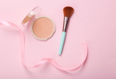 Make-up powder box and brush with pink ribbon on pink background. Top view
