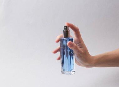 Woman's hand holds bottle of perfume with blue liquid on gray background