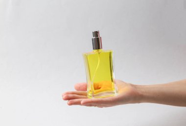 Woman's hand holds bottle of perfume with yellow liquid on gray background