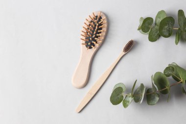 Eco, natural, plastic free. Bamboo toothbrush and wooden hair brush with eucalyptus sprig on gray background