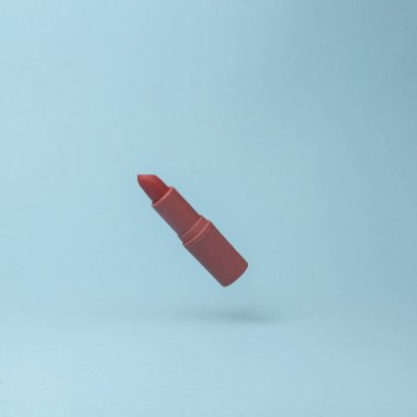 Red lipstick tube flying in antigravity on blue background with shadow. Levitation object in the air. Beauty and fashion concept. Creative minimal layout