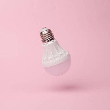 Light bulb flying in antigravity on pink background with shadow. Levitation object in the air. Creative minimal layout