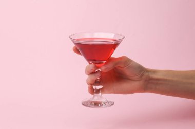 Party concept. Hand holding cocktail glass on pink background