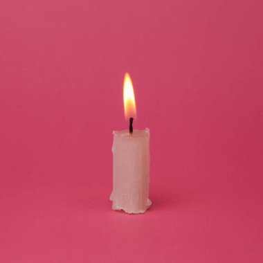 Flaming wax candle on a pink background