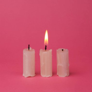 Flaming wax candle on a pink background