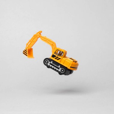 Miniature toy excavator flying in antigravity on gray background with shadow. Levitation object in the air. Creative minimal layout