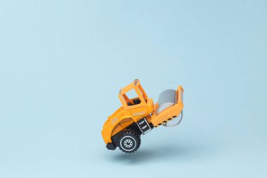 Miniature toy asphalt paver flying in antigravity on blue background with shadow. Levitation object in the air. Creative minimal layout